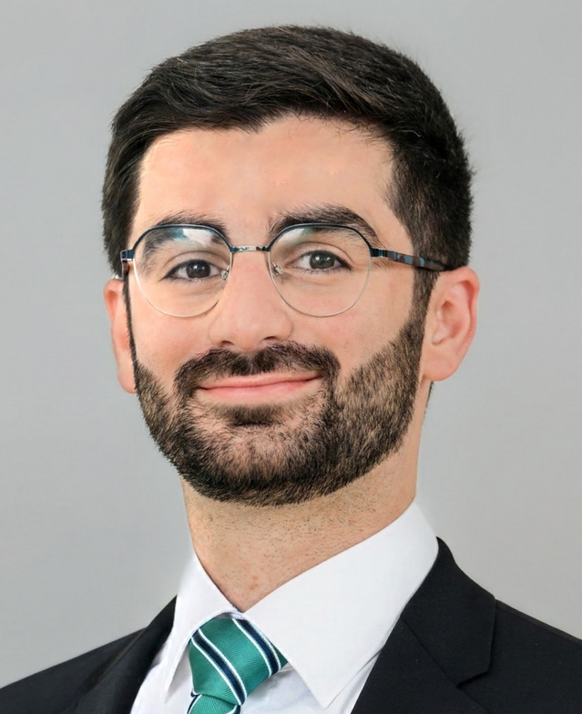 A man in glasses and a suit smiling at the camera